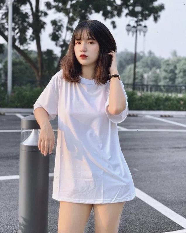 Cô gái trẻ với mái tóc đen dài, mặc áo sơ mi trắng, nhìn thẳng vào ống kính với ánh mắt cuốn hút